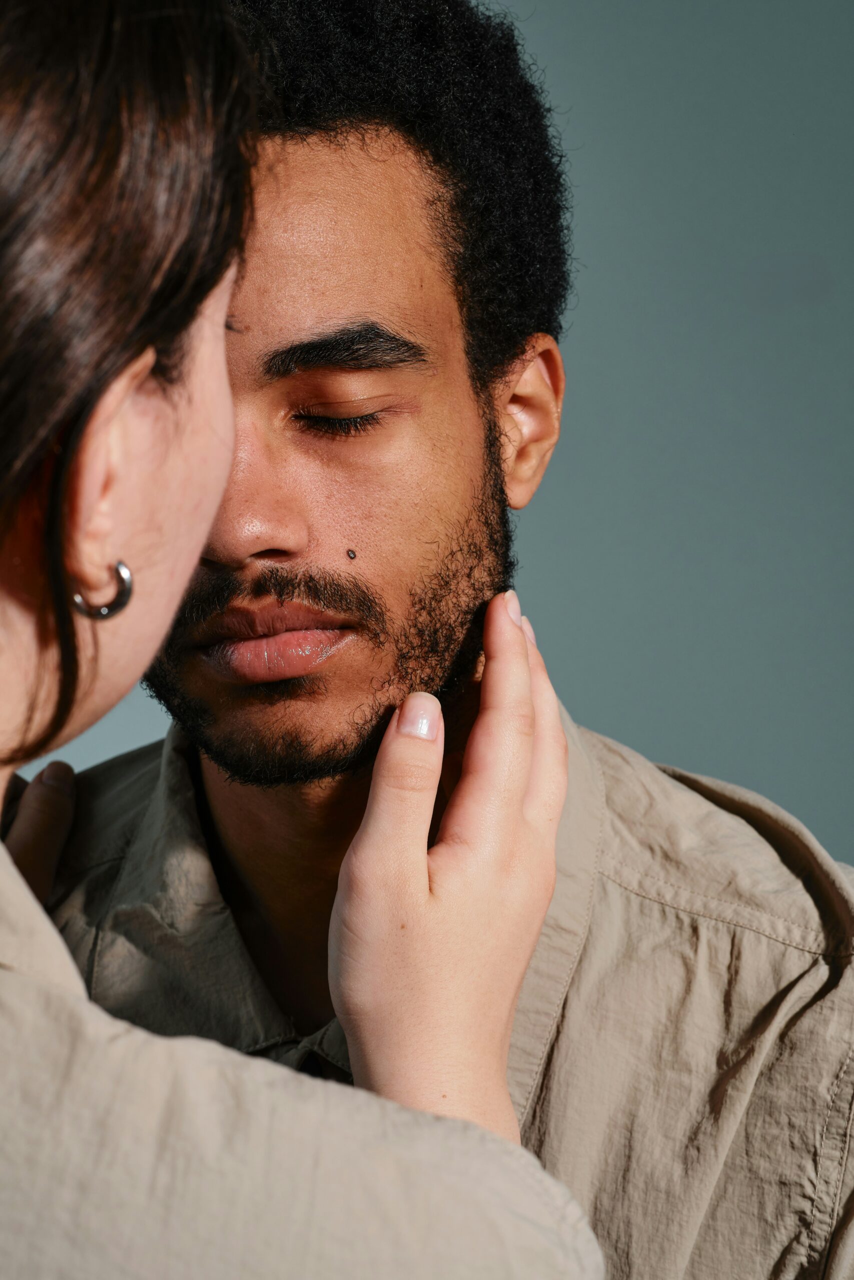 Close-up of a man with eyes closed as a gentle touch rests on his jawline from another person off-camera; calm, intimate moment.
