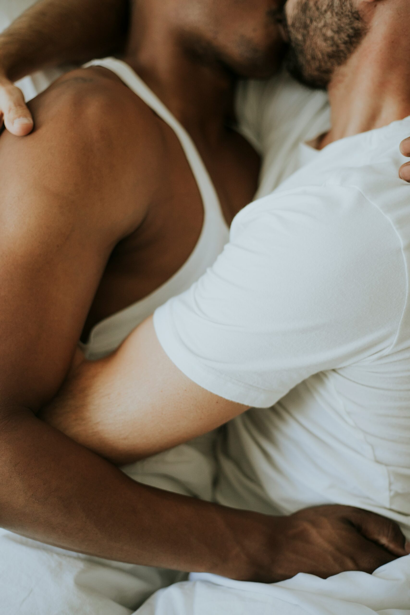 Two people lying in bed, embracing in a close hug with arms around each other.