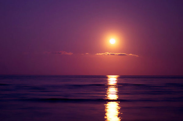 Sunset over a calm ocean with the sun reflecting a bright path on the water.